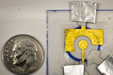 A dime next to a tiny golden electrode.