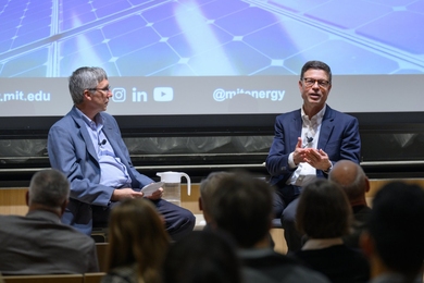 Kurt Kelty speaks on a stage with William Green looking on. Both are seated.