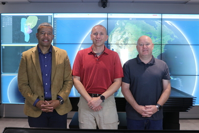 Charles Greene, Lukas Toth, and Duston Mullen pose in front of a bank of nine monitors, six of which display an Earth globe.