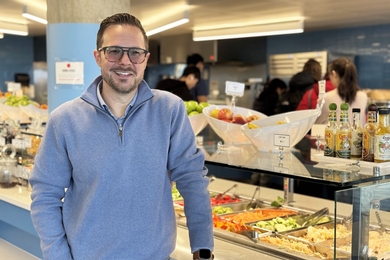 Andrew Mankus posing next to a salad bar in an MIT dining hall