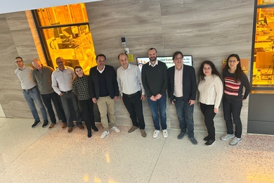 10 people, photographed from an elevated position, pose standing in front of MIT.nano's cleanroom.