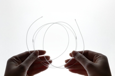Two hands holding a coil of thin, transparent fiber tubing