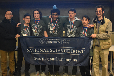 Five students and two coaches hold a banner that says "National Science Bowl: 2026 Regional Championship.” One student has a plush animal on his head