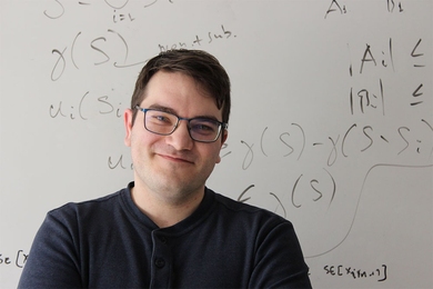Headshot of Gabriele Farina in front of a whiteboard with equations