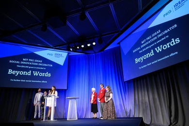 Six people stand on a stage under two screens displaying their team name, Beyond Words