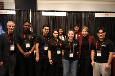 7 MIT students, all wearing lanyards, pose with Governor Maura Healey and MIT’s Stu Schmill