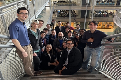 20 people pose on a staircase, photographed looking down from the top step