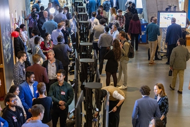 Elevated view of a poster session shows dozens of people milling about. 