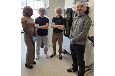 Four people wearing hairnets and nitrile gloves stand in a lab.