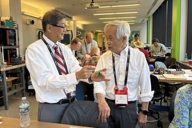 Gim Hom chats with one of his classmates at their 55th-year reunion over a working electronics bench. 