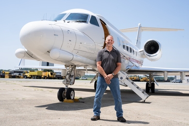 Craig Rowe poses in front of an aircraft on a tarmac on a sunny day