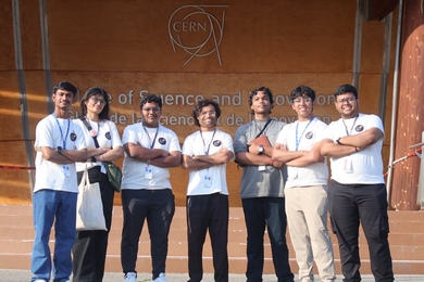 Manu Srivastava and 6 high school students pose standing in front of a sign at CERN with their arms folded