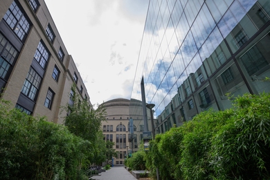 Walkway with a brick building at left and a glass-walled building at right, with the MIT Dome between and beyond them