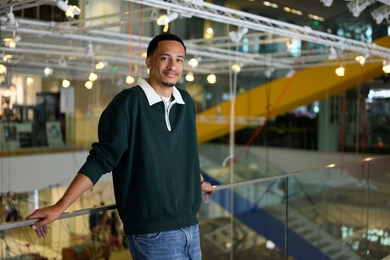 Kayode Dada leans against a glass railing on an atrium walkway
