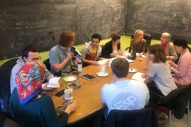 10 people sit around a small seminar table with a blackboard in the background