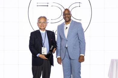 Donté P. Shannon and Hiroshi Ishii pose on stage. Ishii holds a trophy.