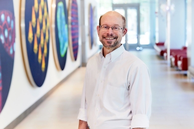 Michael Yaffe stands posing in a hallway decorated with large circular images of scientific art