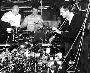 Michael Andrews, Marc-Oliver Mewes, and Wolfgang Ketterle gather around the machine they and their MIT collaborators used to demonstrate the first atom laser. Mr. Andrews and Mr. Mewes are graduate students in physics; Dr. Ketterle is an assistant professor in the department.