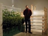 List Center Curator Bill Arning stands beside Monica Bonvicini's Turning Walls, 2001, composed of plants and wooden metal and plastic fencing over a wooden armature.