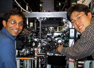 The experimental apparatus that produced the continuous source of Bose-Einstein condensate is shown with two of the graduate students who worked on the experiment. Ananth Chikkatur (left) points to the science chamber, in which the source was made. Yong-Il Shin points to the production chamber where the BECs were produced before being transferred to the science chamber (32 centimeters away) using ...