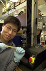 Chemical engineering research associate Yadong Wang stretches a piece of regular vulcanized rubber. Biorubber, which is white and opaque, is stretched using the machine by his side.
