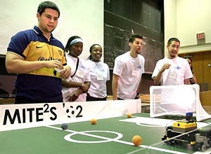 Teaching assistant Guillermo Chicas  (far left), watches the winning robot in action at the 2002 MITE 2S  Robotics Design Competition, held July 26. The team that designed and built the  machine included (left to right, wearing white) Cherelle Walls, Oyinade Aderibigbe,  Aaron Arizpe and Daniel Chaparro.