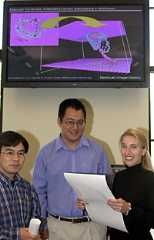 Ting Zhu (left), Ju Li, and Krystyn Van Vliet stand below an image in MIT's NanoMechanical  Technology Lab that is akin to one they included in their paper on predicting  defects in materials.