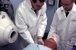 Research Affiliate Stead Kiger (left) and Visiting Scientist Matthew Palmer prepare the patient for therapy. The mask immobilizes the patient's head during treatment.