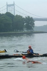 Accompanied by a kayak, Nick Sidelnik swims around Manhattan with the Triborough Bridge in the background.