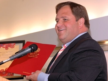 Cambridge Mayor Michael Sullivan praises the work done by Cambridge food pantries during the 13th annual Cambridge First Day celebration, held at MIT on June 7. He is holding one of the Cambridge First Day awards and a bound City Council resolution.