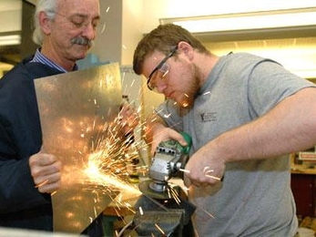 Professor Woodie Flowers of mechanical engineering helps senior John Rebula work on part of a manioc grater, designed to grate large quantities of manioc or kasava for food in Haiti. The project is for 2.009, whose final presentations are Monday, Dec. 12.