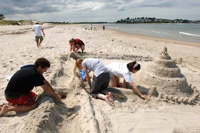 Students construct an elaborate sandcastle during a pre-orientation event held Aug. 24 by the Department of Architecture. From left, freshmen Tom Goff from New Jersey, Ashley Kowall (red shirt) and Renee Reder (blue shirt), both of New Hampshire, and architecture graduate student Victoria Lee work on their creation on Crane Beach in Ipswich. <a onclick="MM_openBrWindow('orientation-1-enlarged.html...