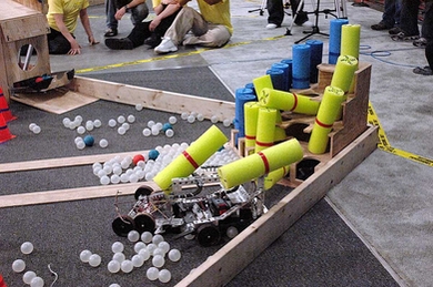 Students robots in this year's 2.007 contest held at MIT competed in performing beaver-like tasks, including knocking down pool noodle 'trees' and dumping them in a ping-pong ball 'river,' to score points.