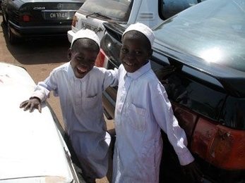 Two children in their best clothes climb between the cars in a gridlocked parking lot.  In the Bamako market cars are often parked three or four deep, and leaving means waiting for the owners of the cars in front of you to finish shopping. <a onclick="MM_openBrWindow('rotch-1-enlarged.html','','width=509, height=583')">
<span onmouseover="this.className='cursorChange';">
<strong>Open image gallery...