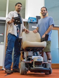 Nicholas Roy, left, assistant professor of aeronautics and astronautics, and Seth Teller, professor of computer science and engineering, stand next to the robotic wheelchair they co-designed, which can be navigated by vocal command.