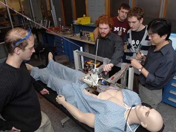 Senior Paul Blascovich watches surgical robot operating from left, while teaching assistant Lael Odhner plays with arm. Junior Tony McDonald watches from back, Junior Ian Rust and instructor Harrison Chin watch from center and right of "patient."