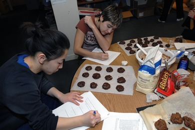Senior Angie Chiang, foreground, and junior Taylor Williamson write notes on the chemistry they have learned by making "Death by Chocolate" cookies in Patti Christie's Kitchen Chemistry course, offered in the ESG kitchen.