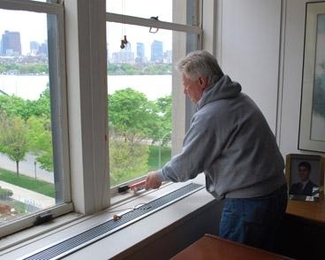 MIT Sloan School of Management Dean David Schmittlein uses caulk to seal up the windows in E52 to help conserve energy.