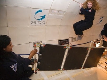 MIT student Tina Srivastava unfolds a solar panel during the micro-gravity flights, while senior Jillian James floats above.