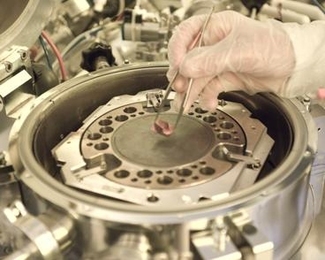Graduate student Will Chung displays a hybrid chip being developed in Professor Tomas Palacios' lab. The machine in the background is used to combine the semiconductor materials into one chip.