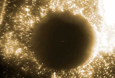 A tiny metal bead suspended in an electric field is just visible in the middle of a hole drilled through a circuit board. The hole itself is only the diameter of the wires used to connect circuit elements on the circuit board.