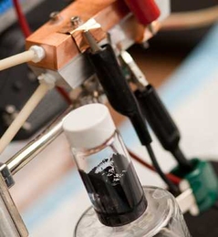 A sample of 'Cambridge crude' — a black, gooey substance that can power a highly efficient new type of battery. A prototype of the semi-solid flow battery is seen behind the flask. 
