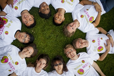 Students lying on their backs in a circle, with heads in the center, photographed from above
