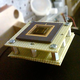 A new energy harvesting device converts low-frequency vibrations into electricity. The device, the size of a U.S. quarter, is shown mounted on a stand.
