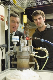 Professor Donald Sadoway and Materials Processing Center Research Affiliate David Bradwell observe one of their small test batteries in the lab. The battery itself is inside the heavily insulated metal cylinder at center, which heats it to 700 degrees Celsius.