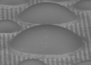 On a surface patterned with tiny pillars (white squares), and with a coating of a lubricant liquid that fills the spaces between the pillars, dome-shaped droplets of water condense but remain free to move quickly across the surface, unlike on conventional flat surfaces or ones with just the patterning, where they tend to stay stuck in place. The new surface treatment could provide a significant bo...