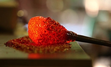 Photo of molten red glass in a blob at the end of a pole