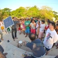 People gathered outside, one of whom is holding up a solar panel