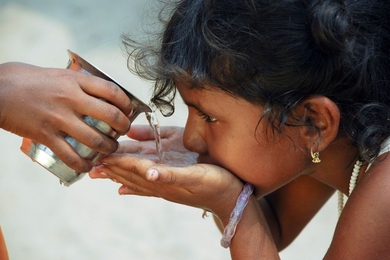 Child cups hands while drinking water flowing through poured cup