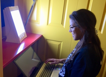 A fourth-year PhD student in electrical engineering and computer science, Ariel Anders works beside a light-therapy box recently installed at MIT.